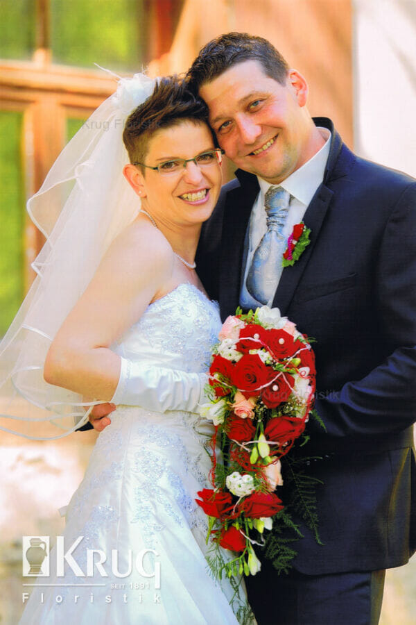 Paar mit Brautstrauß rot-weiß mit Rosen, Freesien, Band und Perlen und Anstecker