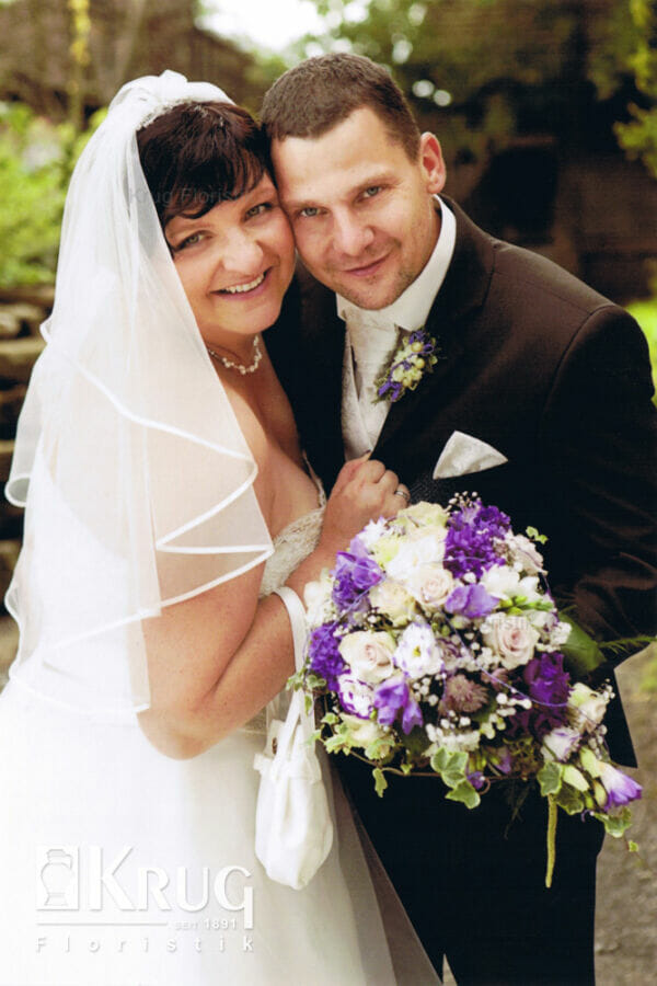 Paar mit lila-weißem Tropfen-Brautstrauß mit Rosen und passendem Anstecker